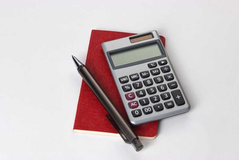 a pen, red paper and calculator on white