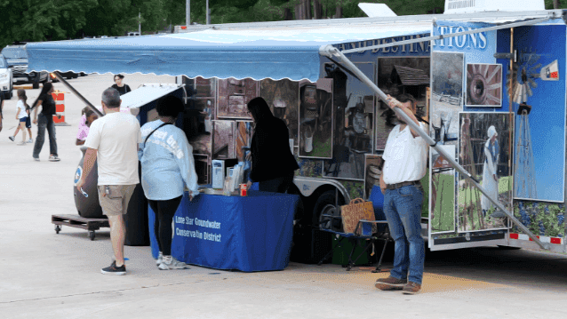 A young boy plays at a water pump station labeled Lone Star Groundwater Conservation District, while an event staff member in a blue shirt assists nearby.