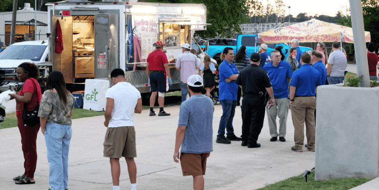 People gather and wait in line at a Southern Slider Co. of Texas food truck parked on a paved area during an outdoor community gathering.